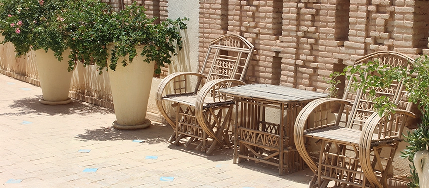 Shaded courtyard at Dar Tozeur with rustic wicker chairs and a table against traditional brick walls.