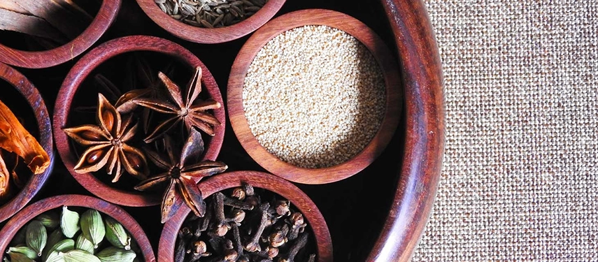 Close-up of wooden bowls filled with colourful Tunisian spices including star anise and cardamom.
