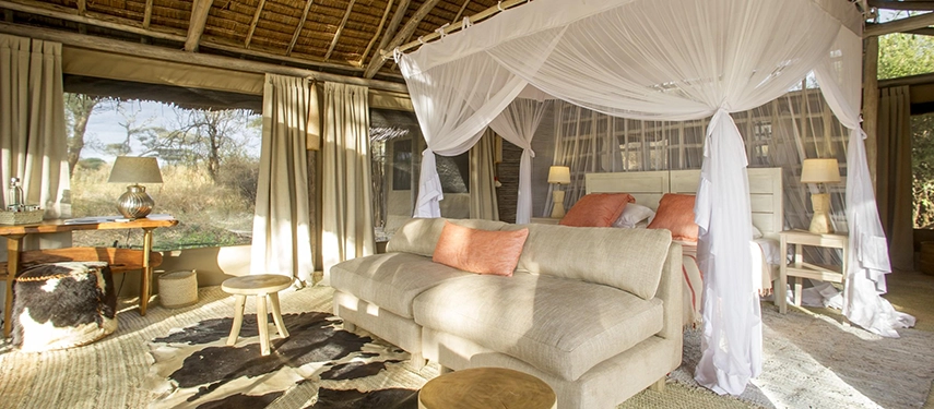 A spacious canvas room with soft natural fabrics, mosquito-draped bedding and warm wooden accents opens to peaceful Tarangire views.