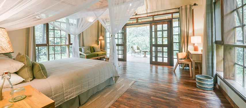 Spacious double room at Primate Lodge Kibale with four-poster bed, sheer mosquito netting, and private deck access.