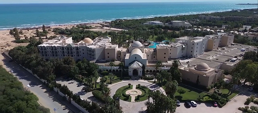 Aerial view of The Residence Douz with its white domed architecture and the Mediterranean coastline beyond.