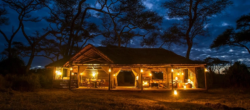 The open-sided mess glows warmly at dusk beneath acacia trees, creating an inviting gathering space in Tarangire’s wilderness.