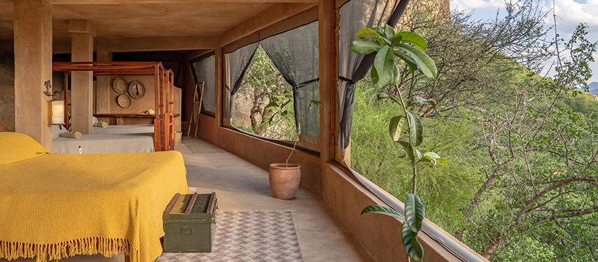 Rustic twin bedroom with natural decor and wraparound mesh windows overlooking the greenery.