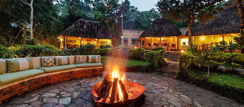 Lit campfire at Primate Lodge Kibale surrounded by stonework and cosy seating, perfect for evening gatherings.