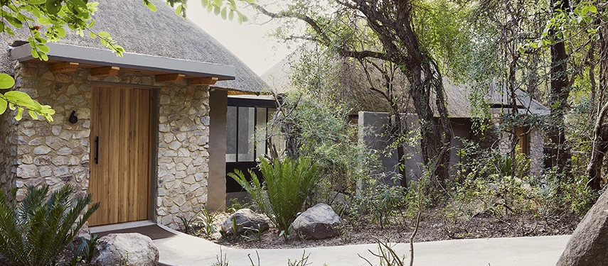 Stone and thatch interleading superior chalets nestled in shaded woodland at Londolozi Founders Camp.