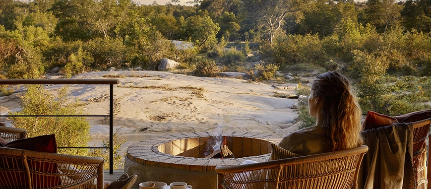 Guest relaxing beside a private firepit on the deck of Londolozi Founders Camp with scenic river views.