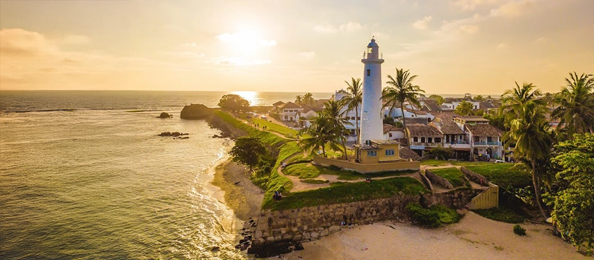 Aerial view of Galle Fort Lighthouse with palm trees and the coastline at sunset in Sri Lanka.