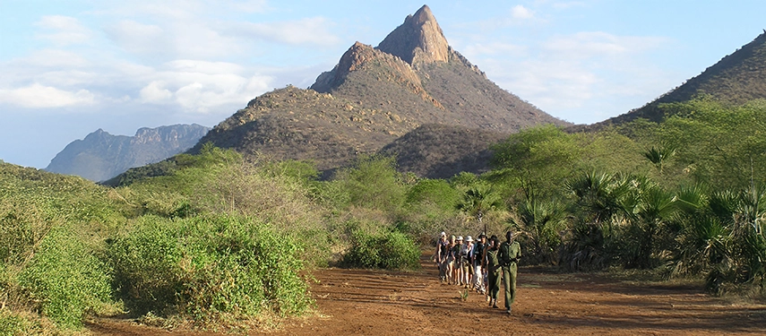 Tourists on a guided walking safari in Kenya with mountains in the background