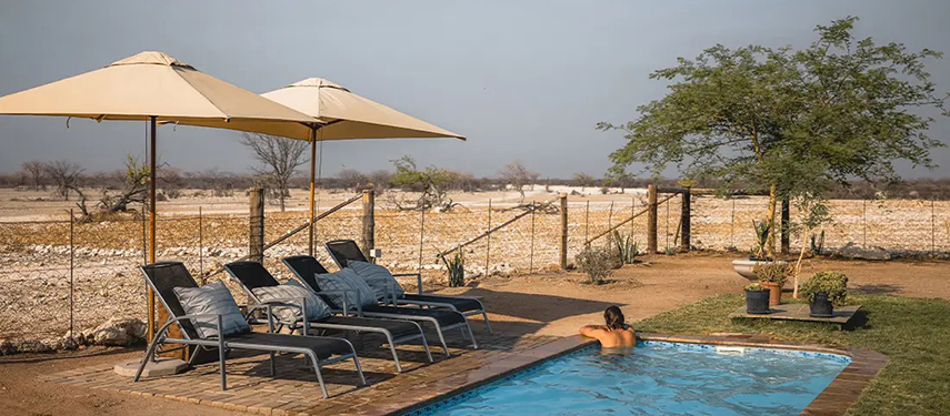 A person relaxing in the swimming pool at Safari House with views across the dry savannah.