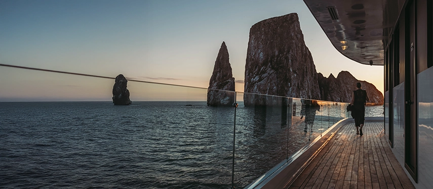 Guest walking along panoramic deck at sunset on the Hermes Galápagos Mega Catamaran.