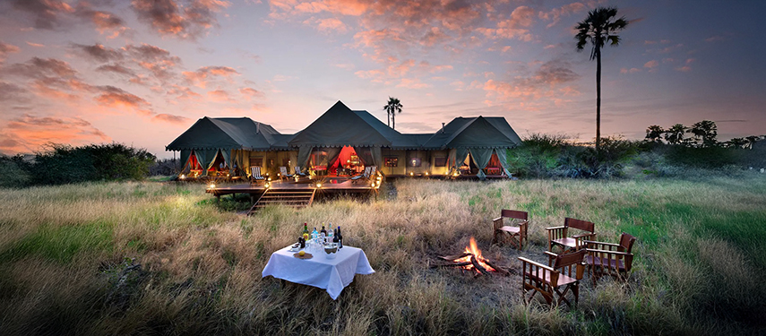 Jack’s Private Camp illuminated at dusk with a firepit and drinks table set up on the grassy plains in front.