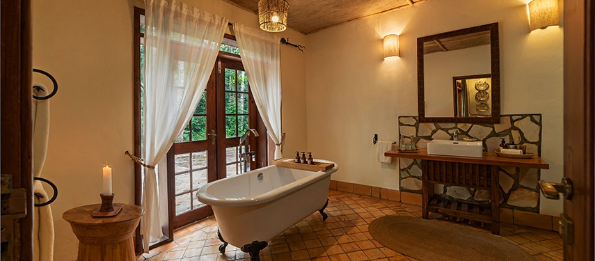 Freestanding claw-foot bathtub in the Honeymoon Cottage bathroom at Primate Lodge, with views into the tranquil forest.
