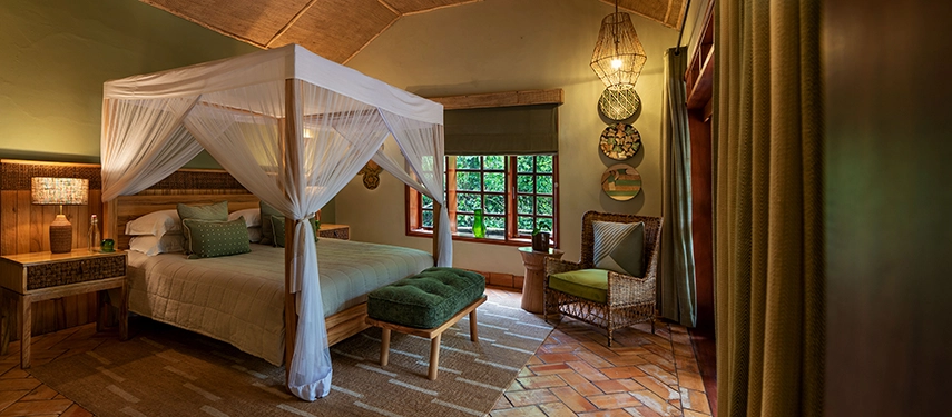 Spacious double bedroom in the Honeymoon Cottage at Primate Lodge with four-poster bed and natural décor inspired by Kibale Forest.