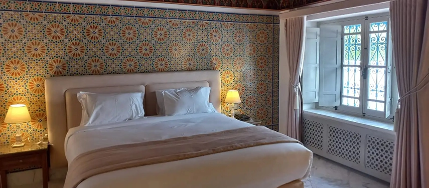 Elegant guest room with intricate Tunisian tilework, soft lighting, and a large comfortable bed.