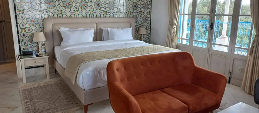 Spacious bedroom featuring patterned Tunisian tiles, a plush bed, and a warm terracotta sofa.