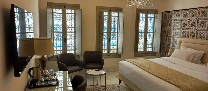 Bright guest room with tiled feature wall, chandelier lighting, and tall shuttered windows.