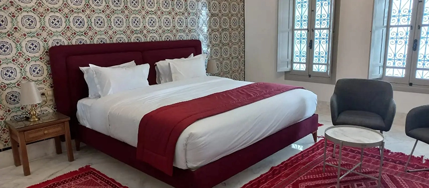 Luxurious bedroom with patterned wallpaper, deep red furnishings, and a bold rug for contrast.