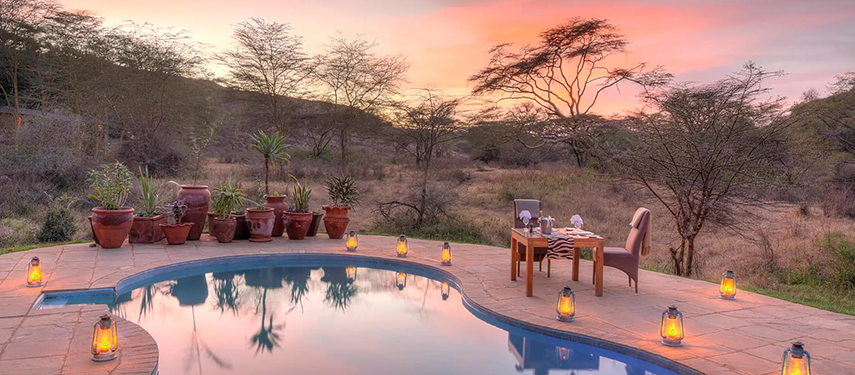 A romantic poolside dining setup with lanterns at sunset, surrounded by bushland near The Emakoko.
