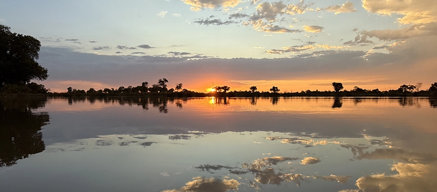 A glowing Okavango Delta sunset reflects across still floodwaters, capturing the serene beauty that defines evenings at Beagle Expeditions.