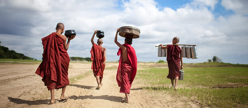 Group of young Buddhist monks in red robes walking across open land carrying alms and baskets in Sri Lanka.
