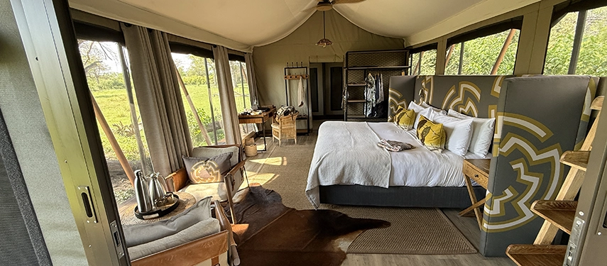 Inside a Karangoma safari tent, a beautifully styled bedroom opens to views of grasslands, combining comfort with an immersive wilderness setting.