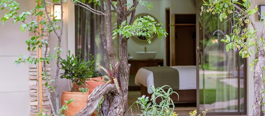 A garden-facing suite at Insika Lodge opens onto lush greenery, blending indoor comfort with the natural calm of the Zambezi River setting.