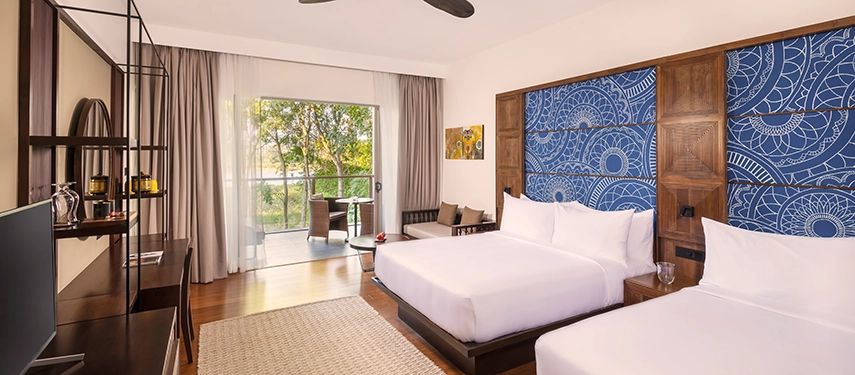 A bright twin room at Jetwing Kandy Gallery features contemporary décor, blue patterned wall panels and a balcony framed by gardens and natural light.