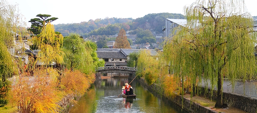 A traditional boat gliding along Kurashiki’s historic canal, framed by autumn colours and Edo-period storehouses.