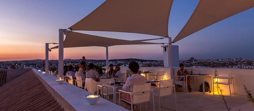 Rooftop restaurant at sunset with guests dining beneath sail shades overlooking Tunis city skyline.