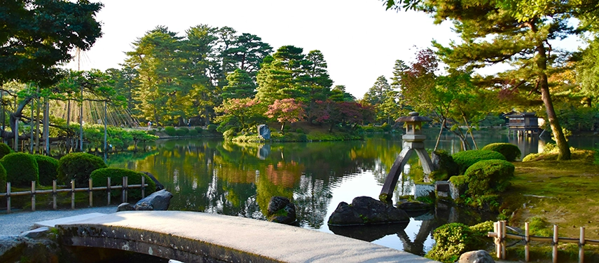 A peaceful garden scene in Kanazawa with still water, stone lanterns and manicured pines reflecting traditional aesthetics.