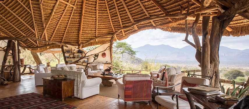 A rustic open-air lounge at Sarara Camp with natural timber beams, white armchairs, and sweeping views of the Mathews Range.
