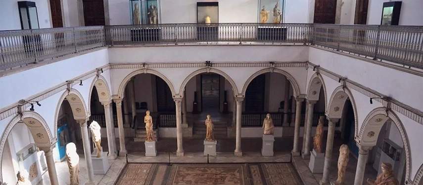 Interior of the Bardo Museum with Roman statues, marble arches, and an intricate mosaic floor.
