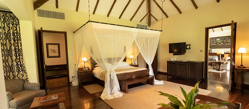 Spacious family cottage at Legendary Lodge in Arusha featuring a king bed with mosquito netting, polished timber floors and warm, light-filled interiors overlooking the gardens.