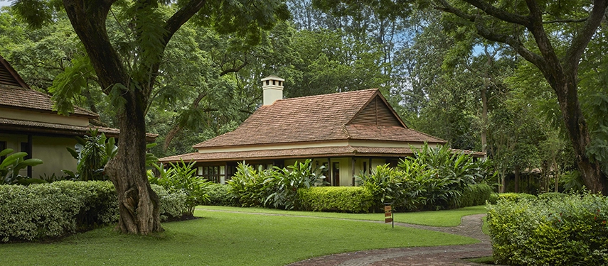 Garden cottage exterior at Legendary Lodge in Arusha, surrounded by mature trees, manicured lawns and lush planting that create a peaceful, private retreat.