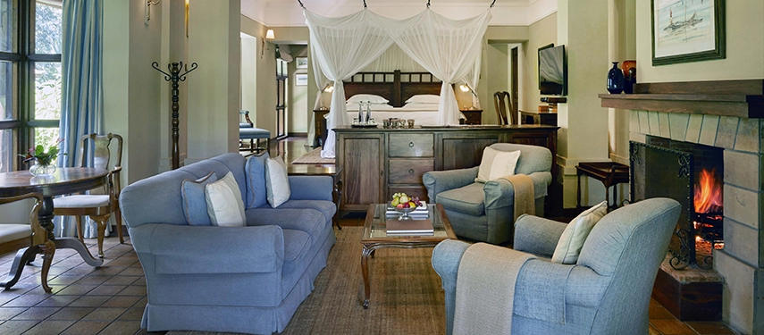 Spacious garden cottage interior at Legendary Lodge in Arusha featuring a comfortable sitting area, fireplace and a canopied bed opening onto the surrounding gardens.