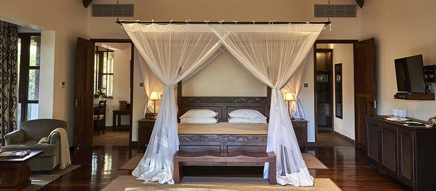Meru Family Room at Legendary Lodge in Arusha showcasing elegant furnishings, a king bed draped in mosquito netting and an open, airy layout opening onto the gardens.