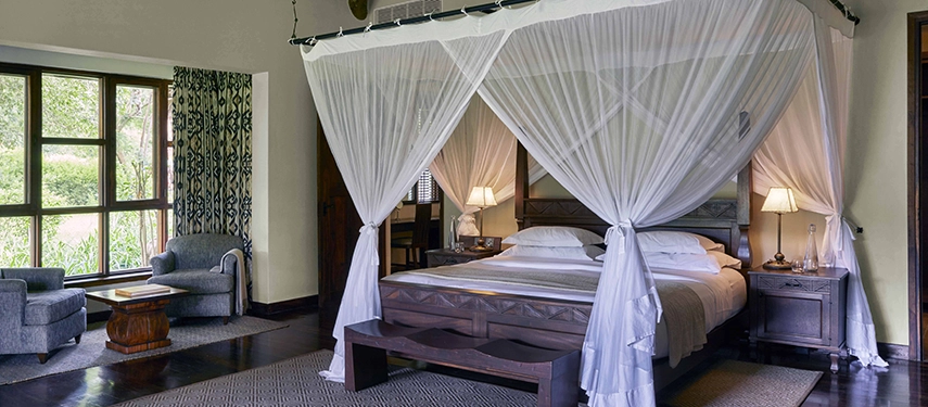 Meru family bedroom at Legendary Lodge in Arusha featuring a king bed draped in mosquito netting, polished timber floors and garden-facing windows creating a calm, elegant space.