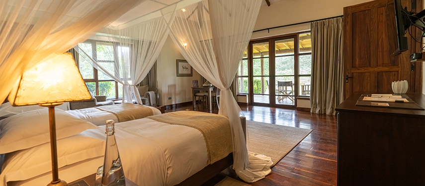 Twin bedroom at Legendary Lodge in Arusha with two comfortable beds under soft mosquito nets, timber floors and large windows inviting in garden views.