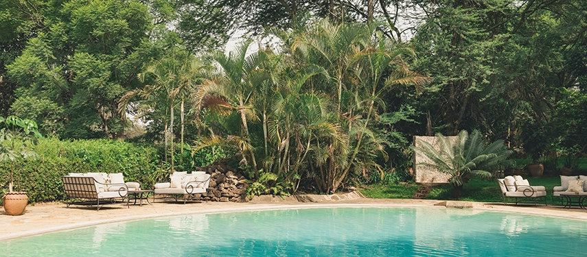 Swimming pool at Legendary Lodge in Arusha set within tropical gardens, with sun loungers and shaded seating offering a relaxed space to unwind between adventures.