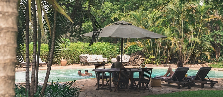 Guests enjoying the pool at Legendary Lodge in Arusha, framed by palms and greenery, capturing the lodge’s laid-back atmosphere and garden setting.