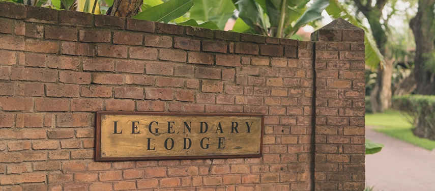 Entrance sign at Legendary Lodge in Arusha set into a brick wall, marking arrival to the lodge’s peaceful gardens and heritage-style main areas.