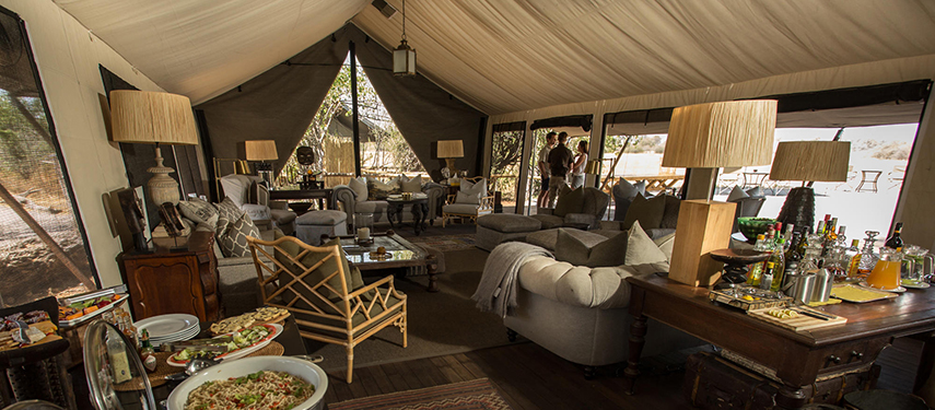 Comfortable main lounge tent at Little Machaba, decorated in vintage safari style with ample seating and a well-stocked drinks station.