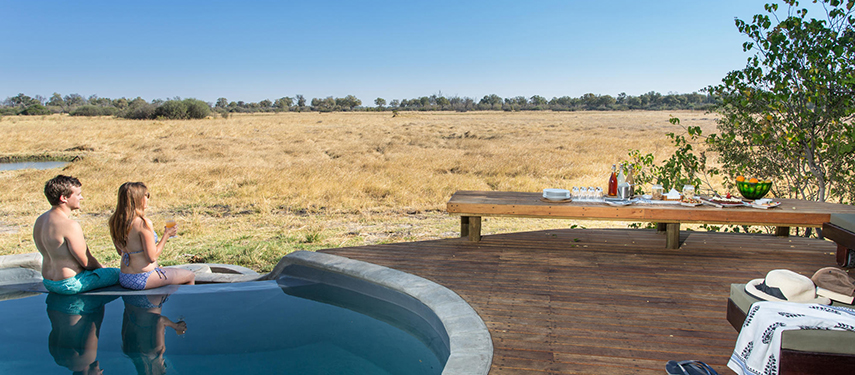 Couple enjoying drinks while seated in a plunge pool overlooking open grasslands from the camp deck.