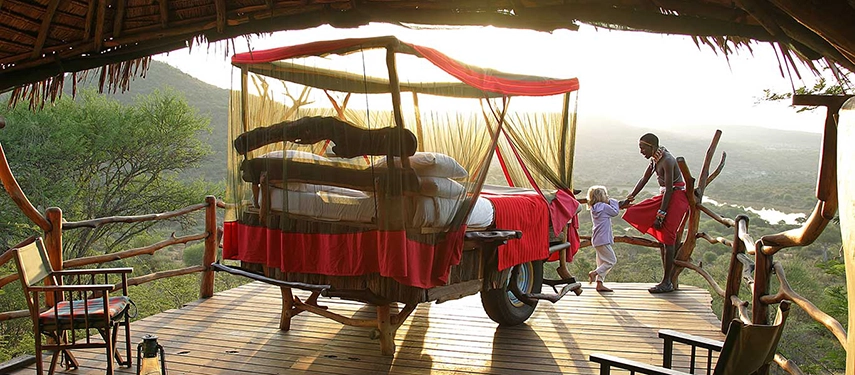 Samburu guide talks to a young guest next to a Loisaba Star Bed with expansive views across Kenyan bushlands.