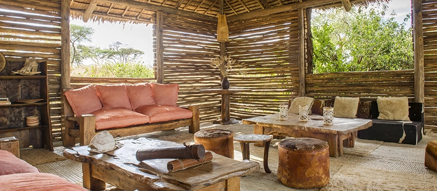 An open-sided lounge with handcrafted wooden furniture and soft cushions offers a relaxed retreat overlooking Tarangire’s bushveld.