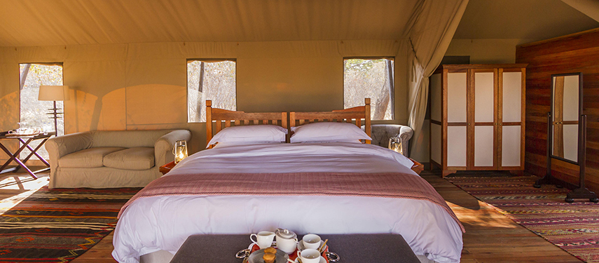 Spacious tent interior featuring a king-size bed, plush furnishings and a large wooden deck with canvas sides.