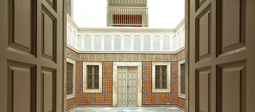 View through open doors into a tiled courtyard with ornate Tunisian patterns and marble flooring.