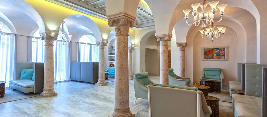 Refined lounge with stone columns, chandeliers, and comfortable seating beneath high arched ceilings.