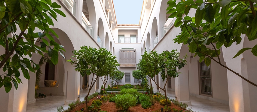 Courtyard garden filled with greenery, framed by arched balconies and white walls.