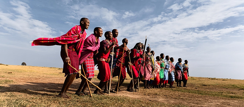 A group of Maasai men and women in vibrant red and pink shukas perform a traditional dance on the open plains of the Mara North Conservancy, Kenya.